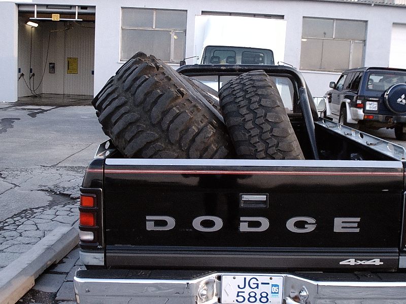 Rear of black Dodge 4x4 pickup with two off-road tires in the bed