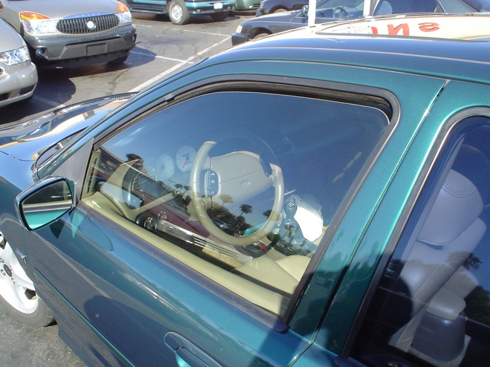 Green sport coupe at a dealer lot showing tan interior through window