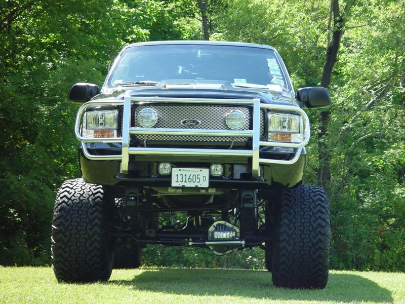 Lifted black Ford Excursion SUV, front view, chrome brush guard, big tires, on grass.