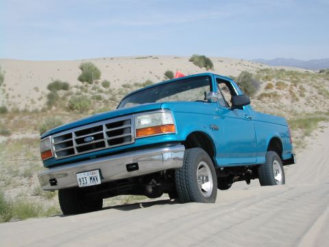 1994 Ford Bronco - 1994 Ford Bronco navigating sand dunes under a clear sky.