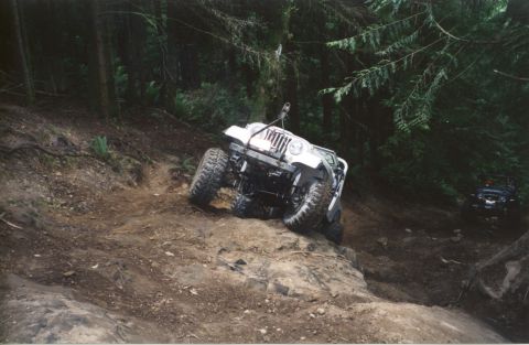 1990 Ford Bronco - A white Jeep Wrangler navigates a steep, off-road trail with another vehicle visible in the background.