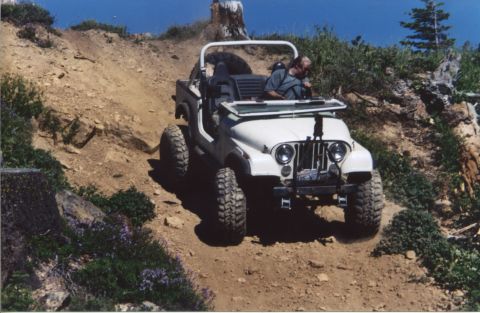 1990 Ford Bronco - A white Jeep CJ-7 navigates a challenging off-road trail with steep inclines and rocky terrain.