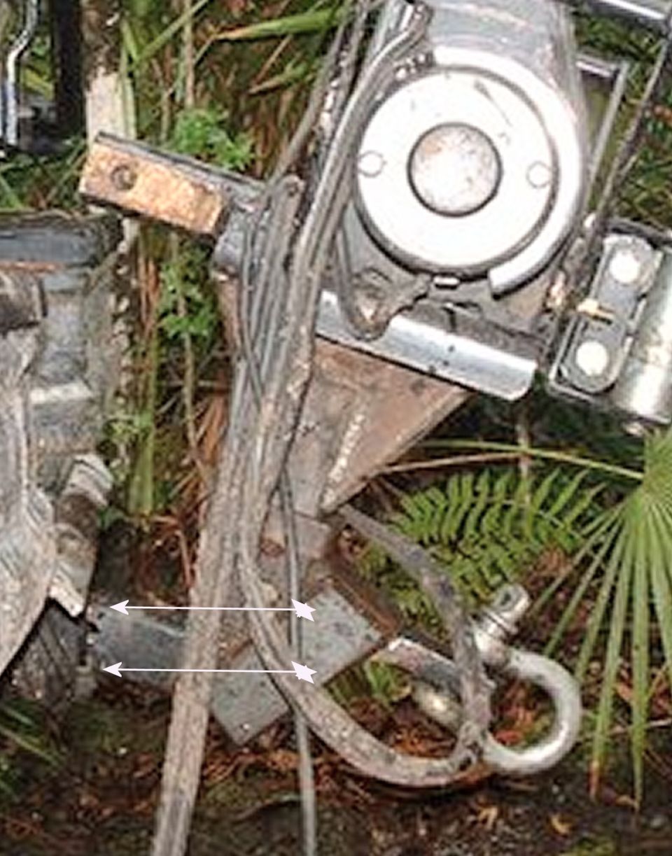 Close-up of a winch mechanism and a tow hook, likely from a vehicle, with some greenery in the background