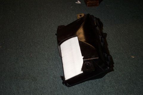 1998 Ford Crown Victoria - A black plastic air filter housing with a white filter element is shown on a dark carpeted surface.