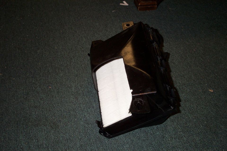 Black plastic air box with white pleated air filter on green carpet