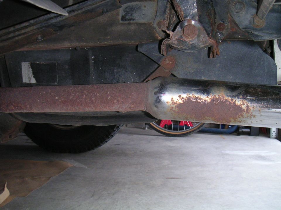 Rusty exhaust pipe and muffler seen from under a vehicle on a garage floor