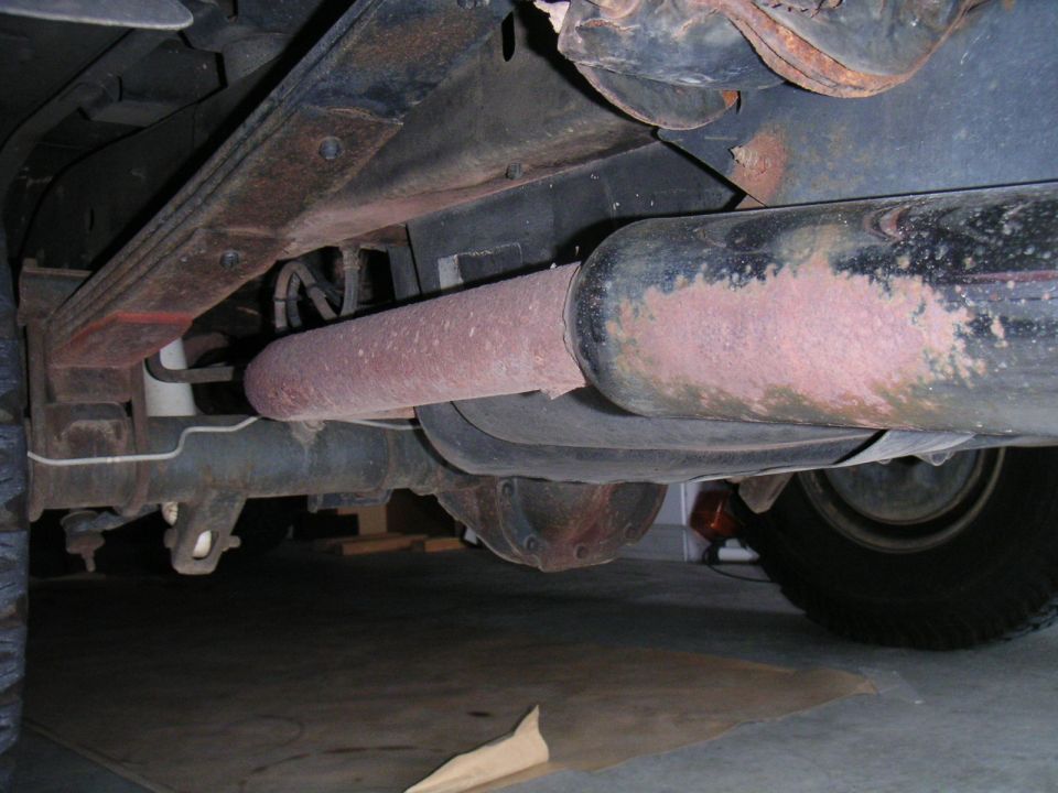 Rusty muffler and tailpipe under a truck beside the leaf spring and rear axle