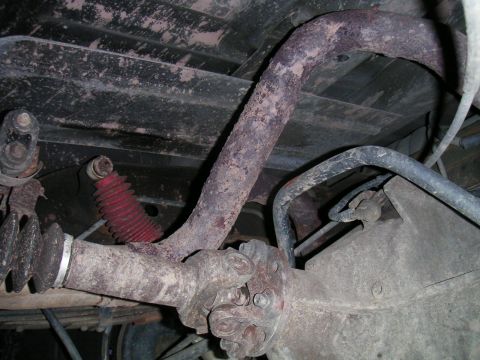 1994 Ford Bronco - Undercarriage view of a solid rear axle showing the driveshaft and U-joint bolted to the pinion yoke of the differential housing, with a ru…