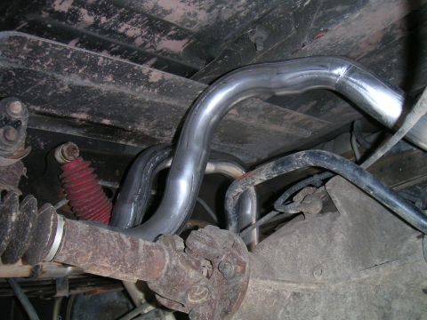 1994 Ford Bronco - Underbody view of newly installed bright mandrel-bent exhaust pipes routed over a rear axle, with a rusty driveshaft and U-joint entering t…