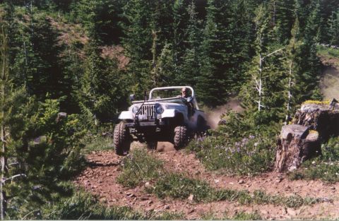 1990 Ford Bronco - White Jeep CJ-7 navigates a dusty trail through a forest, with a driver visible.