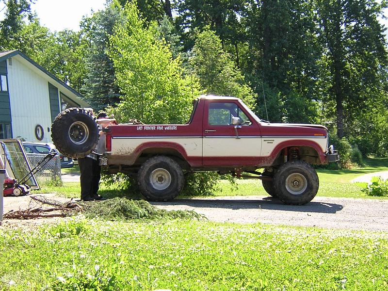 Lifted red and white Ford Bronco on big mud tires parked on gravel driveway
