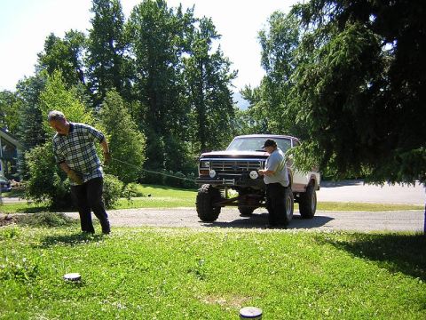 1985 Ford Bronco - A man pulls a rope connected to a heavily modified pickup truck parked on a gravel driveway.