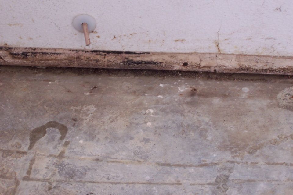 Concrete floor and white wall with mold staining and a wall pipe fixture