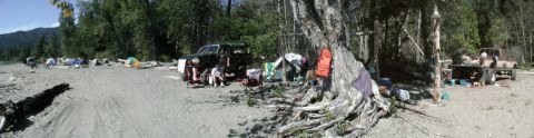 1993 Ford Bronco - A black SUV is parked on a sandy beach, surrounded by tents and trees, with another truck visible in the background.