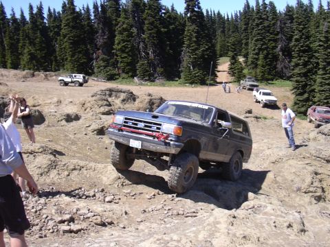 1991 Ford Bronco - A 1991 Ford Bronco navigates a challenging off-road course, with other vehicles and spectators visible.