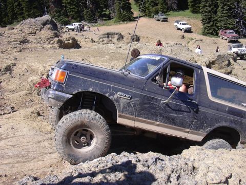 1991 Ford Bronco - A black 1991 Ford Bronco tackles a challenging off-road course with other vehicles visible in the background.