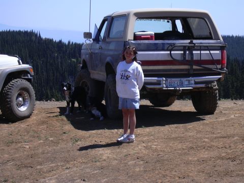 1991 Ford Bronco - A girl stands next to a lifted Ford Bronco with two dogs nearby, overlooking a forest.