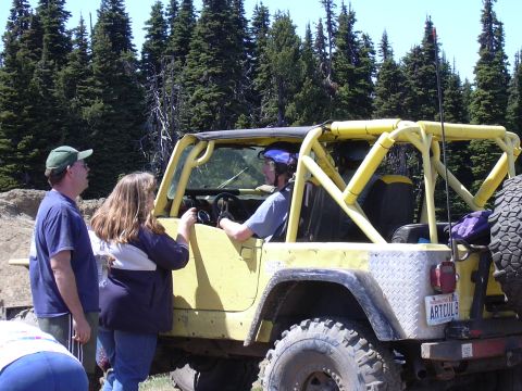 1991 Ford Bronco - A yellow Jeep Wrangler with a roll cage is parked outdoors with people standing around it.