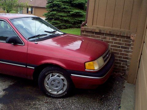 1999 Ford Taurus - This red sedan is parked very close to a brick wall, showing its front quarter panel and driver's side door.