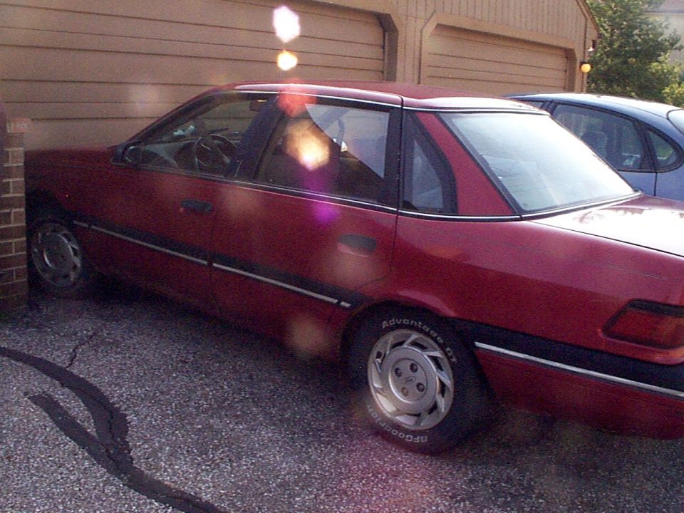 Red sedan side view, parked by garage. BFGoodrich tires visible