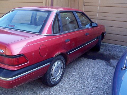 1999 Ford Taurus - Rear quarter panel view of a red sedan, exhibiting rust damage near the wheel well.