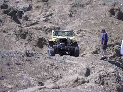 1991 Ford Bronco - A yellow Jeep CJ navigates a rocky, off-road landscape under a clear sky.