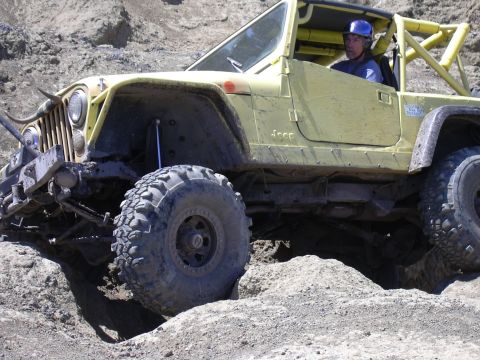 1991 Ford Bronco - A yellow Jeep with a roll cage and large off-road tires is shown navigating a challenging dirt track.
