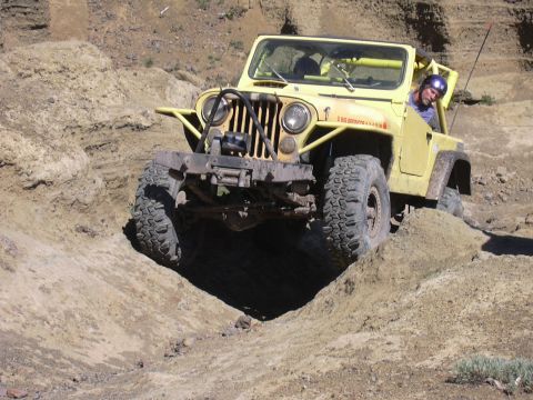 1991 Ford Bronco - A yellow Jeep navigates a steep dirt incline during an off-road excursion.
