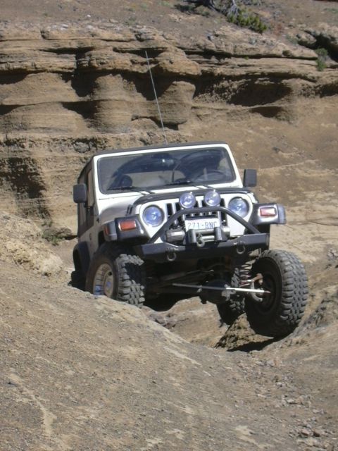 1991 Ford Bronco - White Jeep Wrangler tackles a challenging off-road course with large tires and a lifted suspension.