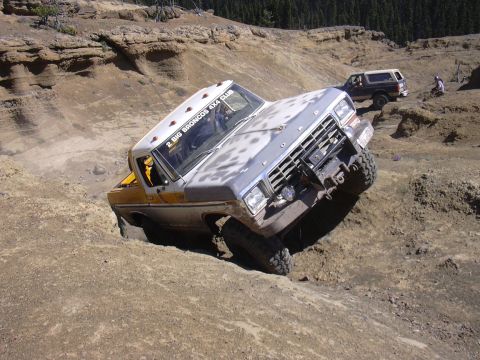 1991 Ford Bronco - A Ford F-Series truck navigates a steep dirt incline, with another SUV visible in the background.