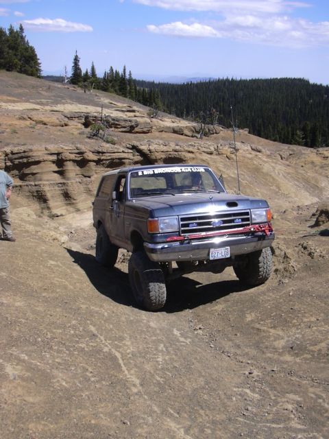 1991 Ford Bronco - 1991 Ford Bronco navigating a challenging off-road course in a mountainous, wooded area.