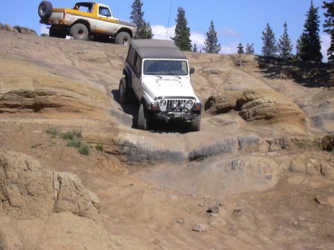 1991 Ford Bronco - Two off-road vehicles navigate a steep, rocky trail under a clear blue sky.