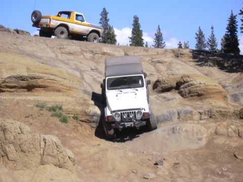 1991 Ford Bronco - Two off-road vehicles navigate a rocky trail under a clear blue sky.