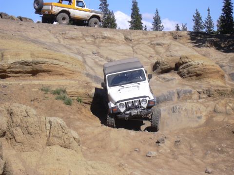 1991 Ford Bronco - Two off-road vehicles navigate challenging rocky terrain under a clear blue sky.