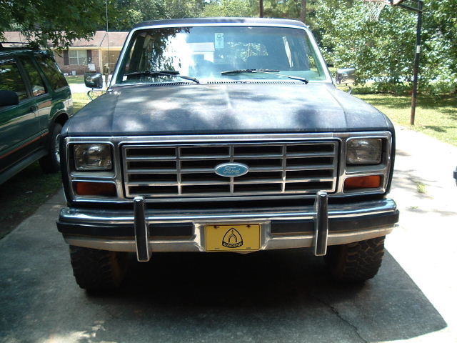 Dark blue Ford Bronco front view, dusty hood, chrome grille, yellow license plate