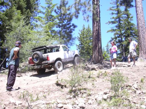 1991 Ford Bronco - A white 1992 Ford Bronco navigates a dirt path surrounded by trees, with people watching.