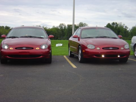 1998 Ford Taurus - Two red 1998 Ford Taurus sedans are parked in a lot under a cloudy sky.