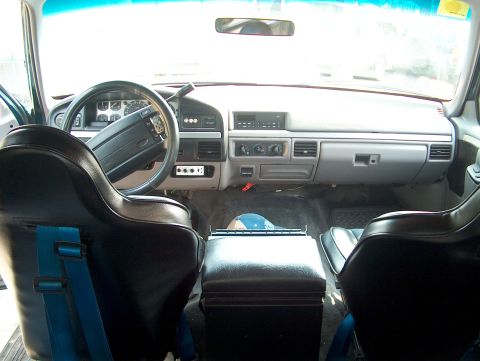 1994 Ford Bronco - The interior of a teal vehicle, black racing seats and a grey dashboard, is viewed from the back seat.