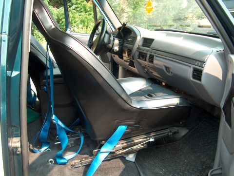 1994 Ford Bronco - The interior of a vehicle is shown, focusing on the driver's seat and dashboard area with blue seatbelts.