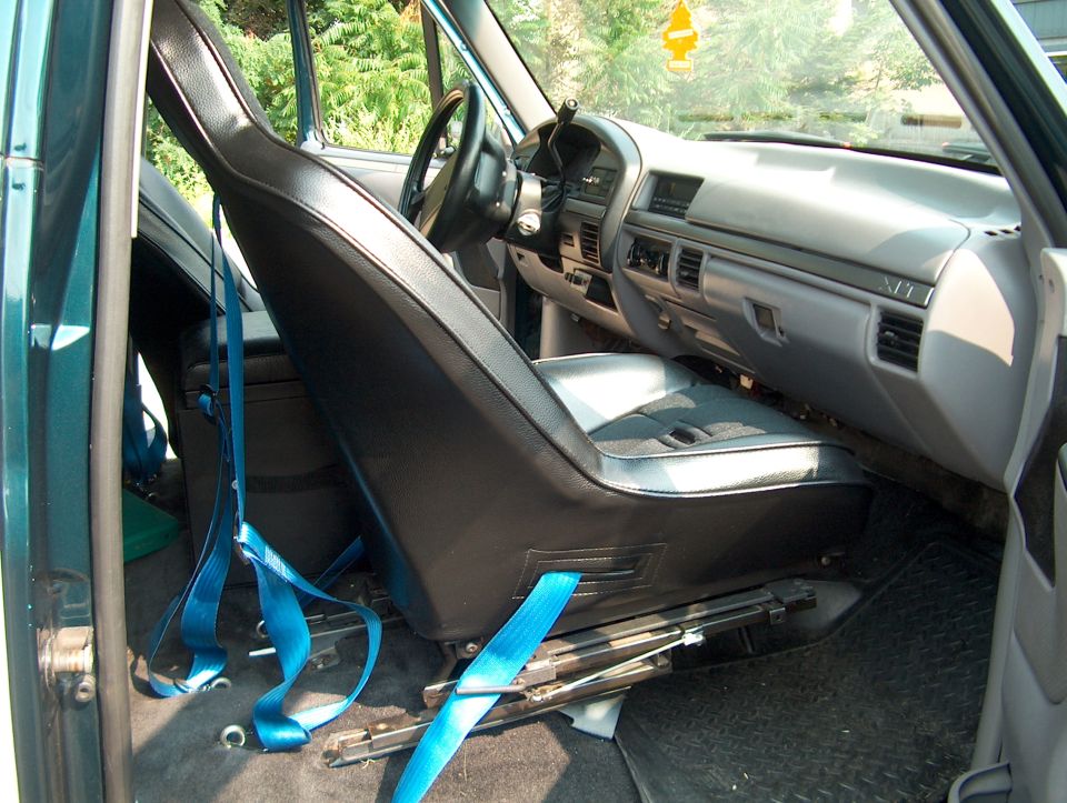 Teal Ford truck interior with gray seat tipped forward exposing seat track and blue seat belts