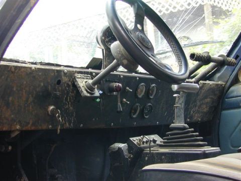 1985 Ford Bronco - The interior of a vehicle shows a worn dashboard, steering wheel, and gear shifter, covered in dirt and grime.