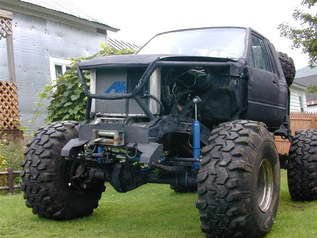 Black modified truck with oversized tires, exposed engine, and a winch
