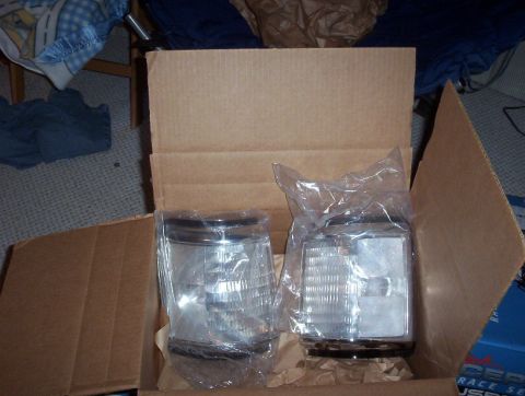 1989 Ford Bronco - Two new headlight assemblies are shown packaged inside a cardboard box.