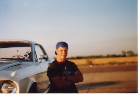 1968 Ford Mustang - A man poses with a classic car, possibly a 1967 Ford Mustang, in an outdoor setting with a field and clear sky.