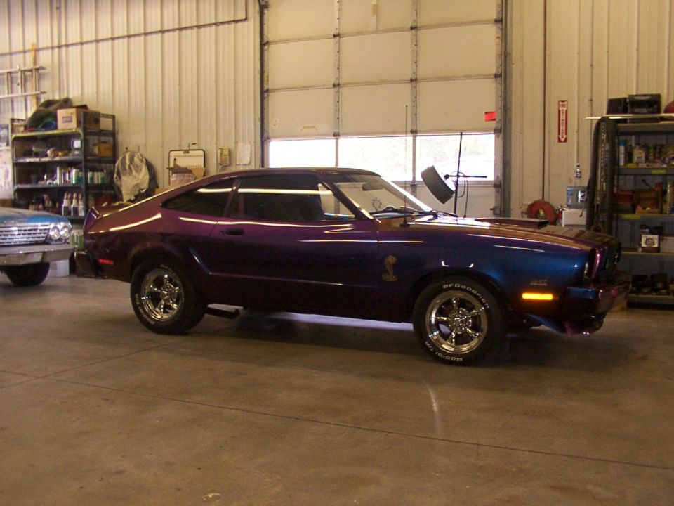 Purple and blue coupe with cobra emblem on fender, parked in garage next to another car