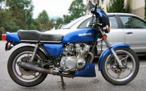 1985 Ford Crown Victoria LTD - A blue Suzuki motorcycle is parked in front of a silver car.