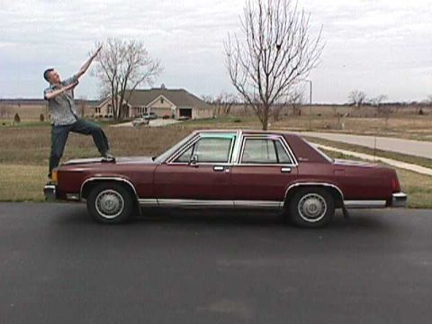1985 Ford LTD Crown Victoria - A person stands on the hood of a maroon sedan parked on a driveway.