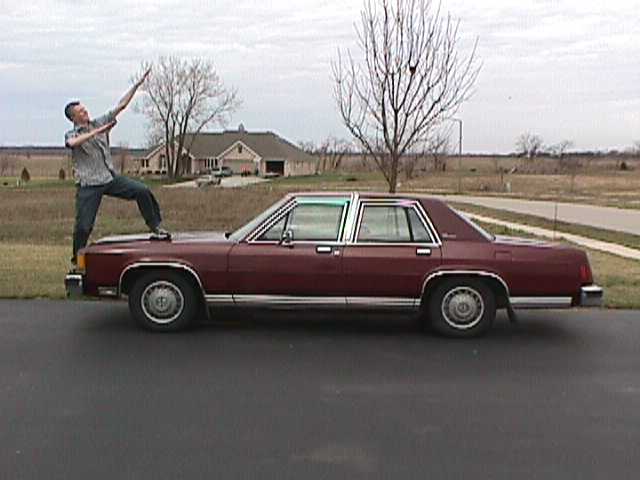 Maroon sedan, looks like a late 70s or early 80s model, with a guy posing on the hood
