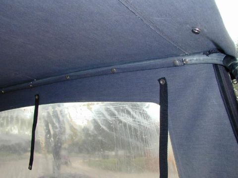1979 Ford Bronco - Interior view up at the underside of a gray fabric soft top, showing the seam and snap studs along a bow tube where the top attaches. Below…
