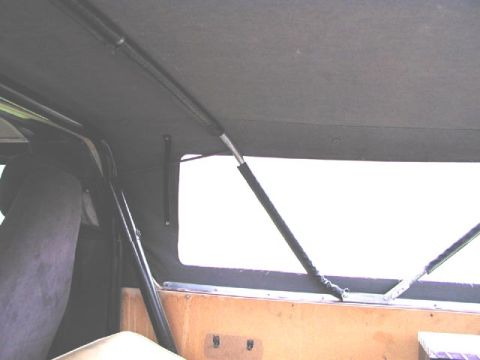 1979 Ford Bronco - Interior shot from the cab looking back into the covered cargo area under a gray soft top, showing black tubular bows and a diagonal suppor…